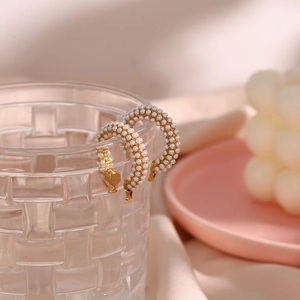 Close-up of gold-plated C-shaped hoop earrings with inlaid white pearls on glass