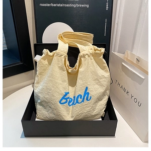 Detail of a beige canvas tote bag with blue Beach lettering in a black display box