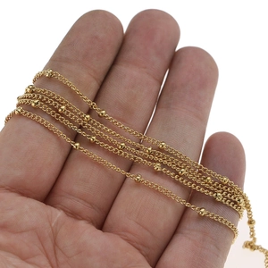 Delicate gold beaded chain for DIY jewelry making wrapped around hands on white background