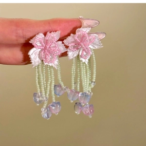 Detail of pink resin flower earrings with colorful beaded fringe held by hand
