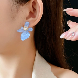 Gros plan d'une boucle d'oreille fleur en résine bleue avec zircon portée par un mannequin
