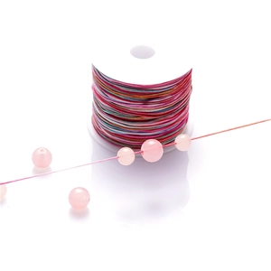 Detailed macro of rainbow gradient cord spool with smooth translucent pink beads for DIY