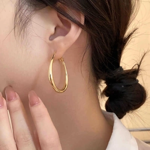 Detailansicht minimalistischer goldener ovaler Creolen, getragen von einem Model