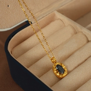 Gold stainless steel necklace with oval black stone pendant in a beige jewelry box