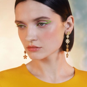 Détail de boucles d'oreilles marguerites asymétriques dorées 18k sur un mannequin