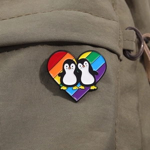 Close-up of heart enamel pin with rainbow stripes and cute penguins on canvas