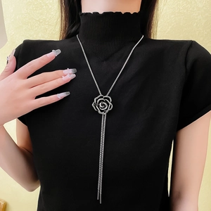 Detail of a black camellia flower necklace with long tassels on a knitted garment