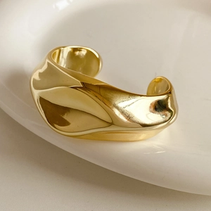 Detail of a high-polish golden twisted cuff bracelet featuring an organic wavy design