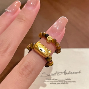 Tiger eye beaded stretch rings with gold cat and coin charms on a hand, Maillard style