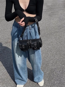 Close-up of black cylinder bag with metal buckles, rings and woven strap detail