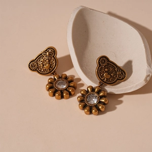 Vintage gold bear and sunflower earrings with zircon stones on a beige background