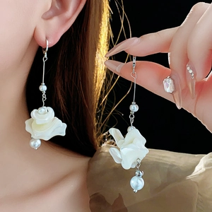 Dettaglio dei orecchini a fiore in madreperla bianca con eleganti nappe di perle lucide