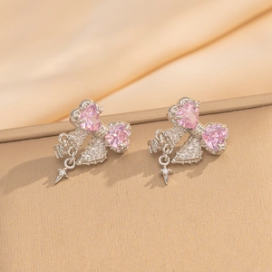 Detail of silver bow earrings with pink heart gemstones and dangling star charms