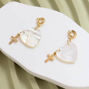 Macro detail of heart-shaped mother of pearl pendant with gold relief and cross charm