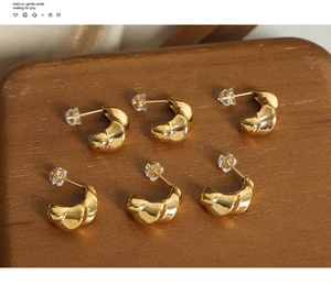 Detail of three pairs of golden twisted rope croissant earrings on a wooden display