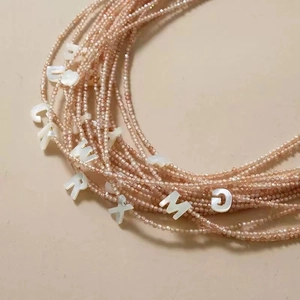 Close-up of pink beaded necklace layers with white shell alphabet beads and crystal accents
