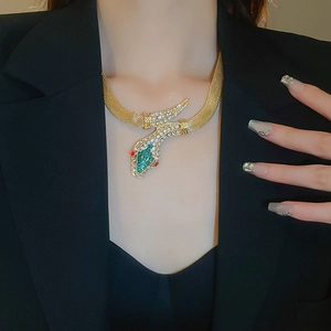 Detailed close-up of golden snake necklace with green and clear rhinestone settings