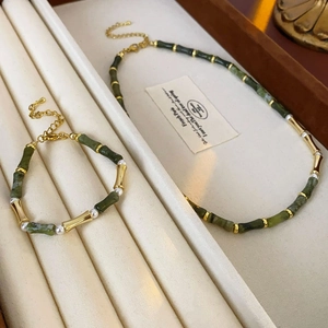 Detail of green bamboo-shaped necklace and bracelet set with white pearls on beige tray