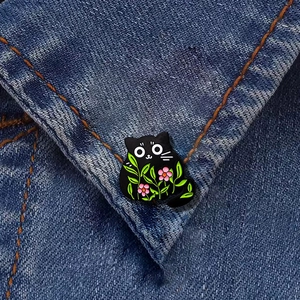 Cartoon black cat enamel brooch with green leaves and pink flowers on denim jacket