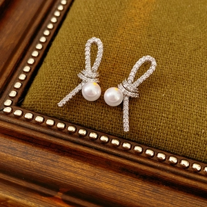 Gros plan de boucles d'oreilles nœuds en argent avec zircons et perles sur velours