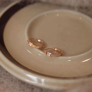 Detail of rose gold braided huggie earrings with small square zircon stones in ceramic tray