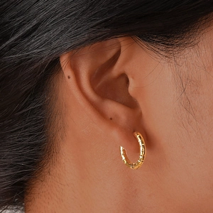 Detailed close-up of golden diamond-cut stainless steel hoop earrings on ear