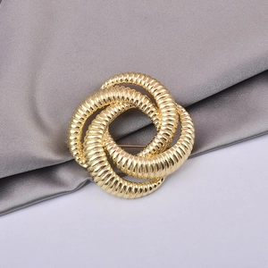 Detailed close-up of a gold spiral knot brooch with textured finish on gray silk