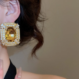 Detailed view of oversized baroque gold earrings with amber stone and clear rhinestones
