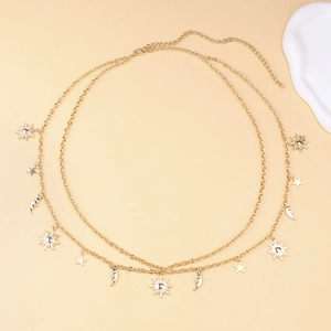 Detail of gold metal waist chain with sun, star, and moon pendants on beige background