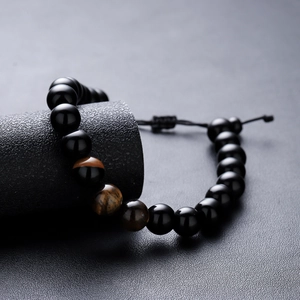 Tiger eye and black beaded bracelet with adjustable woven cord on dark display stand