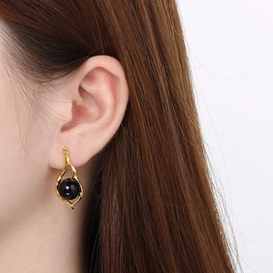 Detail of irregular gold geometric earring with black pearl shown on model's ear