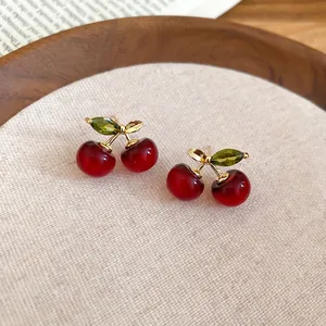 Exquisite cherry stud earrings with red resin stones and gold leaves on linen display