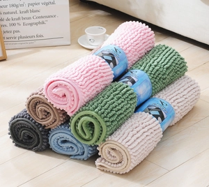 Close-up of rolled colorful chenille bathroom mats with blue packaging bands on wood floor