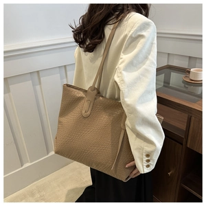 Détail du sac cabas en texture tressée kaki porté à l'épaule par un mannequin chic