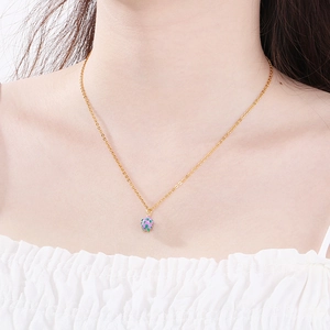 Close-up of a gold chain necklace with a mini pink strawberry pendant on a model