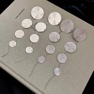 Minimalist gold tassel earrings with textured circular discs on vintage book background