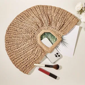 Natural woven straw crescent beach handbag with square handle on a summer holiday background