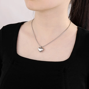 Gros plan d'un pendentif cœur argenté avec chaîne serpent élégante porté par un mannequin