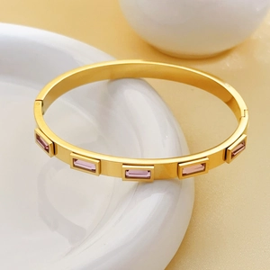 Golden titanium steel bangle with five pink rectangular gemstones on white porcelain