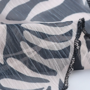 Micro shot of white chiffon maxi dress fabric featuring black leaf patterns and ruffles