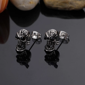Gothic style skull stud earrings for men with black crystals on a reflective surface