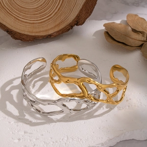 Detail of gold and silver irregular hollow lava open bangles on a stone and wood base