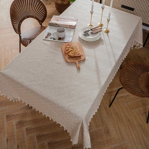 Close-up of beige linen tablecloth with hollow embroidery and decorative tassel trim