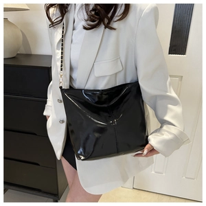 Detail of black glossy leather tote bag with golden chain strap for modern styling