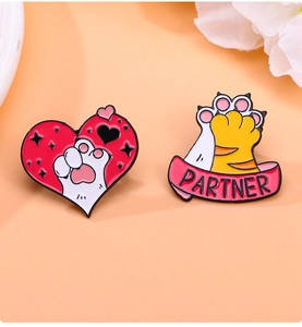 Close-up of pink heart cat paw enamel pins and PARTNER badge on a warm background