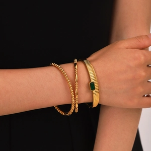 Close-up of gold stainless steel bangle set with vertical stripes and green gemstone on wrist