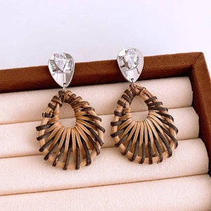 Détail de boucles d'oreilles bohèmes en rotin tressé naturel et puces d'oreilles en zircon