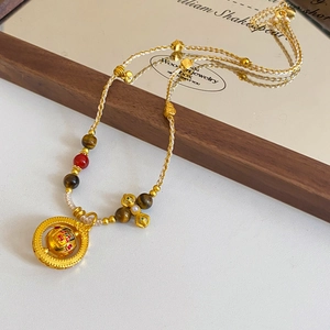 Detailed shot of woven rope necklace with gold beads, tiger eye stone and pearl pendant