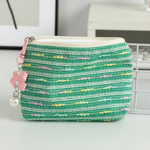 Detailed shot of green woven makeup pouch with pink bow and white pearl pendant
