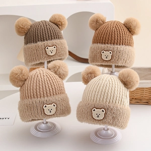 Detailed close-up of winter baby knitted beanies with double faux fur pom-poms and bear patch